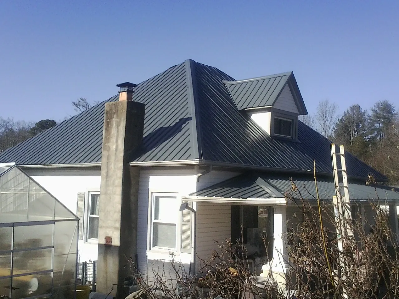Dark blue standing seam metal roof on a white farmhouse with dormer — Slate & Tile Roof Repair by Roofing Brothers in Inwood