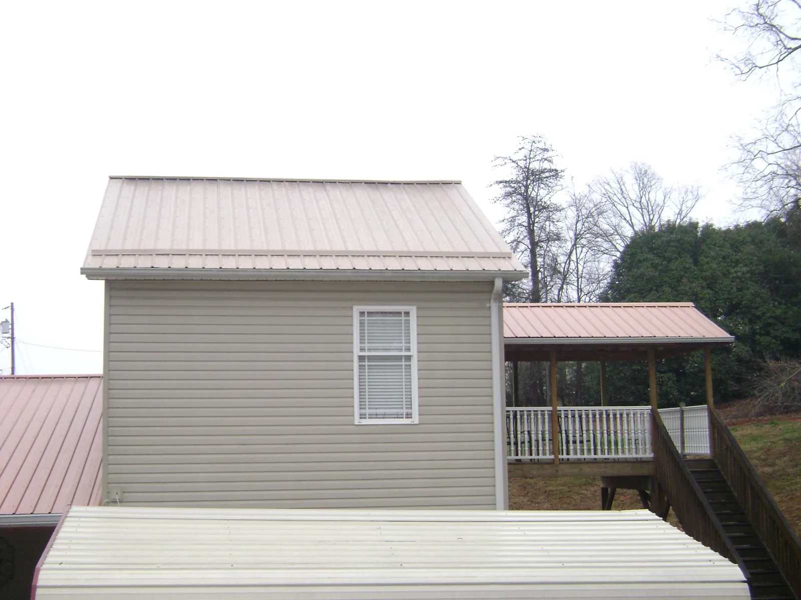 Tan metal roofs on a two story addition and attached porch, from a Roof Replacement job in Inwood